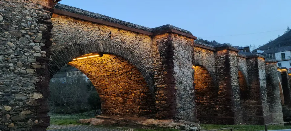 Iluminación LED cálida en los arcos del Puente de Sobradelo, resaltando su estructura de piedra con diseño de Luxes.